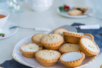 Obraz na płótnie Canvas Traditional english festive pastry mince pies on served for tea time table with lightened christmas tree on background. Cozy home mood. Close up, selective focus. Copy space.