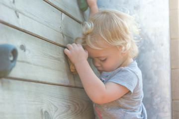 Fototapeta premium Portrait of cute blonde girl climbing plastic boulder wall outdoor.