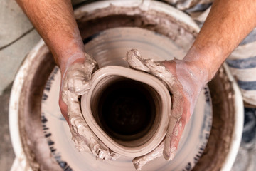 Top view of potter's hand making a vase of white clay on throwing-wheel in ceramics studio, concept...