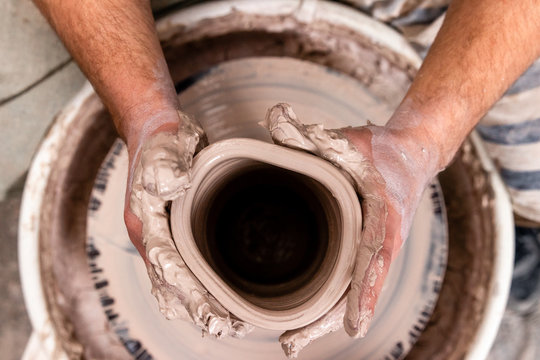Top view of potter's hand making a vase of white clay on throwing-wheel in ceramics studio, concept of creativity and art, horizontal photo, selective focus