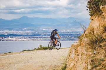 Fototapeta premium young guy riding a mountain bike on a bicycle route in Spain. Athlete on a mountain bike rides off-road against the background of the Mediterranean Sea, Costa Brava. Cycling in Spain