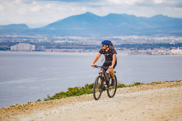 Fototapeta premium young guy riding a mountain bike on a bicycle route in Spain. Athlete on a mountain bike rides off-road against the background of the Mediterranean Sea, Costa Brava. Cycling in Spain