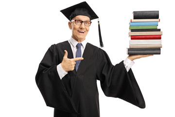 Senior man wearing a graduation gown and holding a pile of books