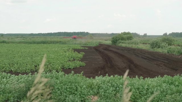 Tractor with special equipment sprays plantings on field.