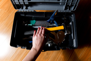female hand with red manicure reaches for tools in an open tool box