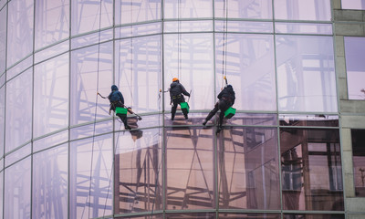 Group of workers cleaning the windows on the high rise building, industrial mountaineers washing the glass facade of a modern office building