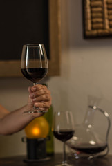 woman hand holding a wine glass over a wood table with bottle, wine container and a old lamp