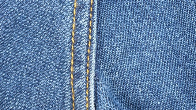 Seam on denim jeans, tracking macro. Denim textile texture. Top view. Slider shot. 4K 422 10 bit