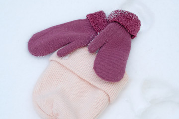 pink knitted hat and two mittens in the snow. Women's hat and warm mittens in winter.