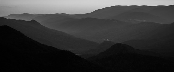 Grey scale shot of the beautiful hills and valleys covered in trees