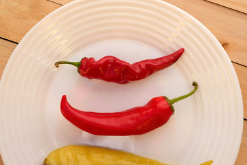 Spicy red pepper on a white plate overlooking the top. Two pod hot peppers on a plate on a wooden background.