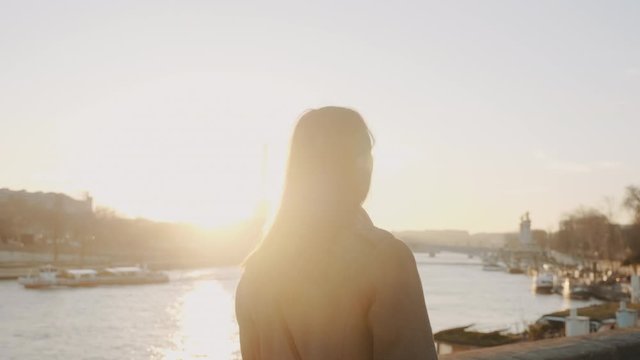 Rear view happy beautiful woman walking along epic sunset Seine river bank on romantic Paris vacation slow motion.
