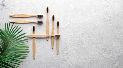 Zero waste, biodegradable bamboo toothbrush on a gray stone concrete countertop with a green palm leaf on the side. The concept of save the planet, ecology, eco. Flat lay with copy space