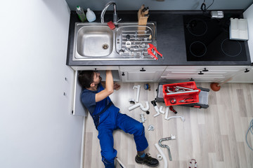 Male Plumber In Overall Fixing Sink Pipe