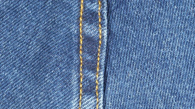 Sliding over seam on blue denim jeans. Denim textile close up, macro. Dolly shot