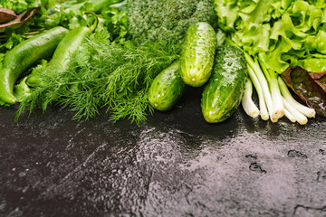 A mixture of fresh produce on a dark table. Dill, green pepper, parsley, cucumbers, broccoli, onions, borax leaves.