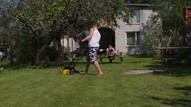 Funny man is mowing lawn by lawnmower, playing harmonica.   Funny, humor, humorous.