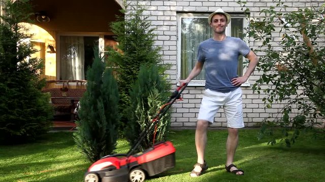 Young man mowing lawn by lawn mower, dancing. Funny, humor, humorous.