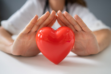 Midsection Of Doctor Protecting Red Heart At Desk