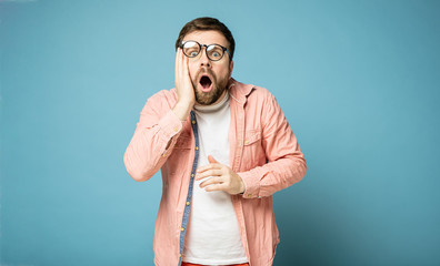 Man in shifted glasses is shocked, he opened mouth, looks at the camera and holds hand to face....