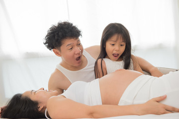 beautiful pregnant woman, her handsome husband and cute little daughter are talking and smiling in bed