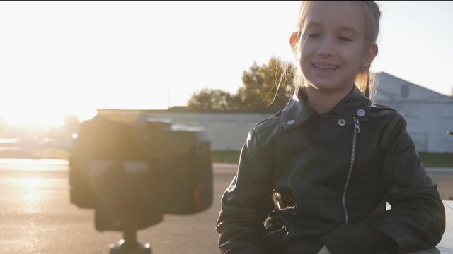 Happy cute little vlogger making online video recording vlog sitting on a park bench. Record vlog and blog concept for Internet.