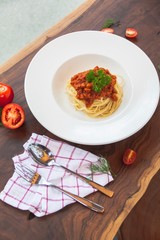 Homemade spaghetti and meat sauce with fresh potatos served in white plate set up with silverware and potatos cut in half on old wood table top