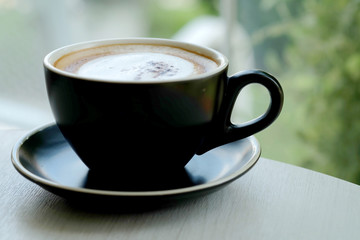 Hot fresh coffee in black coffee cup on table beside glass window near garden and have space for write wording.