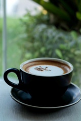Hot fresh coffee in black coffee cup on table beside glass window near garden and have space for write wording.