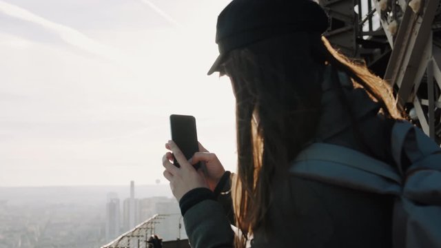 Happy young travel blogger woman taking smartphone photo of Paris view from top of Eiffel Tower on vacation slow motion.