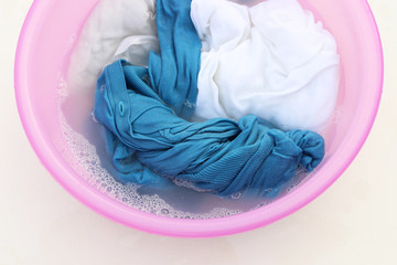 Blue clothes washed with basin with soap bubbles on white background, top view