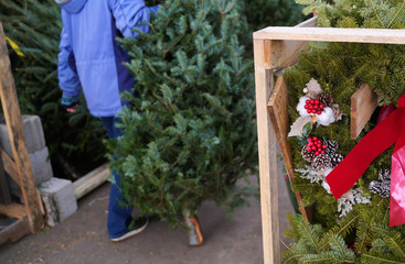 Christmas decorative wreaths, hollies, and red ribbons with browsing shopper carrying tree in the...