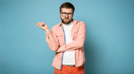 Pompous bearded man with glasses, shows a hand gesture to the side and looks at the camera....