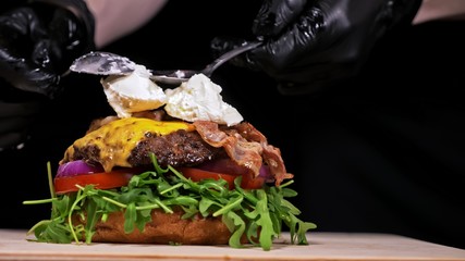 Craft burger is cooking on black background. Consist: sauce, arugula, tomato, red onion, bacon, red...