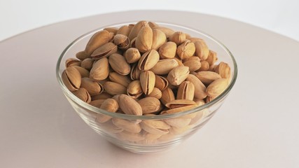 Nuts pistache rotate are on a table in a plate. Snack in transparent dish on an isolated white background are spinning moving. Delicious and healthy protein-rich diet food.