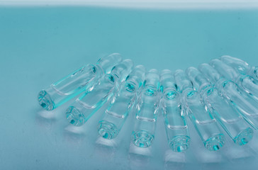 Glass medical ampoule vial for injection. Medicine is liquid sodium chloride with of aqueous solution in ampulla. Close up. Bottles ampule multicolor on background color and water. Human plasma.