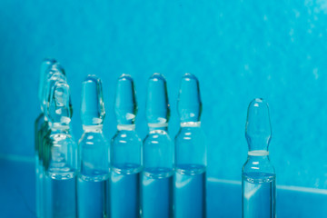 Glass medical ampoule vial for injection. Medicine is liquid sodium chloride with of aqueous solution in ampulla. Close up. Bottles ampule multicolor on background color and water. Human plasma.