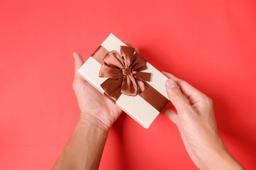 Holding a gift box with two hands on a red background.