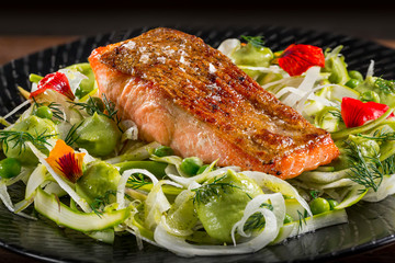 Fillet of freshly grilled salmon fish fillet with avocado and fennal salad on a black plate.