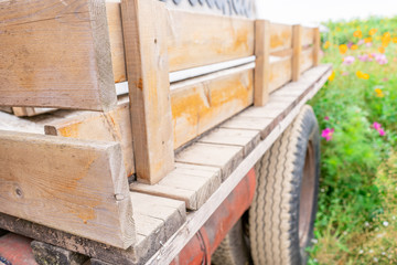 Fototapeta na wymiar Old wooden truck trailer bed with handmade fencing and dirty tire wheel showing in a flower field