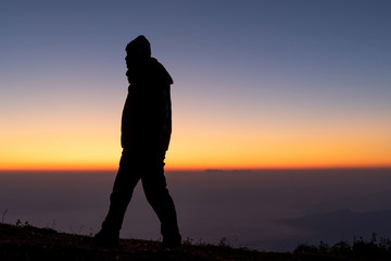 Obraz premium Silhouette man stands alone looking colorful sky in evening time.