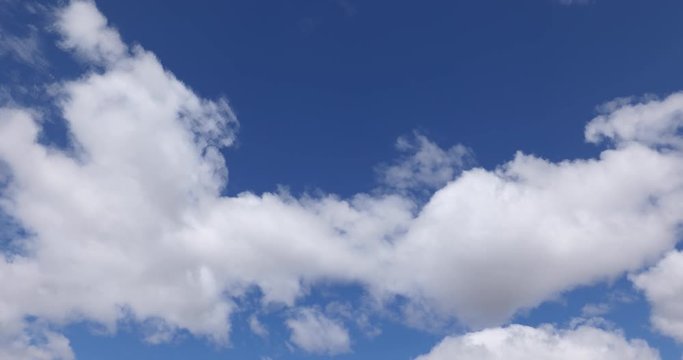 Fluffy white time lapse clouds fly across a deep blue sky with sunny weather in this looping one minute long cloudscape video loop