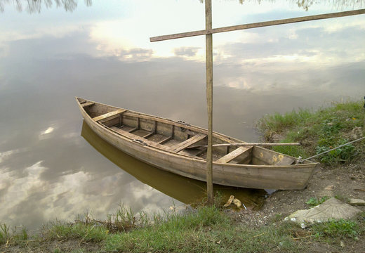 Old wooden boat on the river or lake bank. Boat and reflection of sky. Rowboat. Fishing boat.