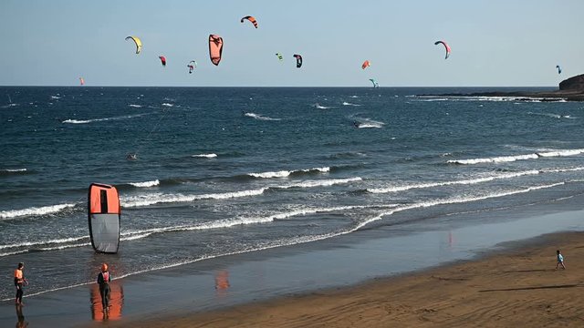 Many colorful kites on beach and kite surfers riding waves during windy day