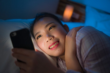 portrait of young beautiful and happy sweet Asian Korean woman with in headband and pajamas enjoying with hand phone in bed at night checking internet social media