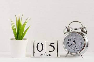 March 5 on a wooden calendar next to an alarm clock and a flower on a white background. Spring in the yard