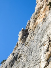 Find alpinist climbing up the steep cliff. Steep rock on the blue sky background with an slightly...