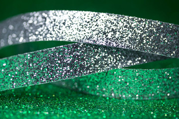 Macro abstract view of sparkling silver holiday ribbons on green glitter background with bokeh