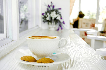 Fototapeta premium Hot latte coffee in a white coffee cup with cookies on white wooden table.