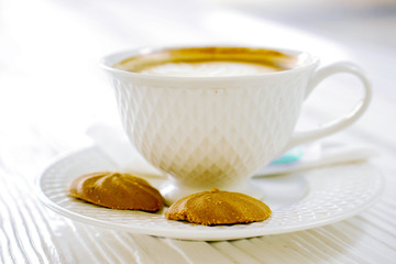 Hot latte coffee in a white coffee cup with cookies on white wooden table.